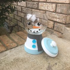 there is a glass bowl with a snowman in it on the ground next to a brick wall