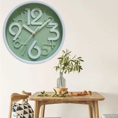 a green clock hanging on the wall above a wooden table with a potted plant