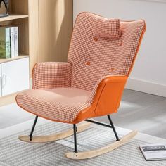 an orange rocking chair sitting on top of a white rug next to a book shelf