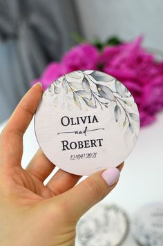 a person holding up a wedding coaster with flowers in the background