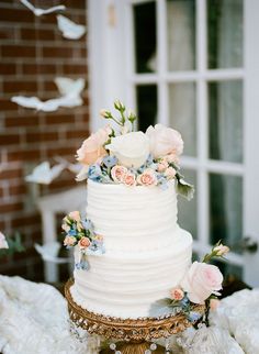 a white wedding cake sitting on top of a table next to a brick wall and window