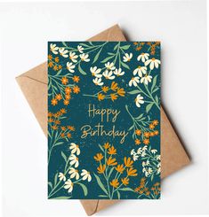 a birthday card with orange and white flowers on it, next to a brown envelope that says happy birthday