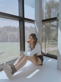 a woman sitting on the floor in front of a window with her legs crossed and holding a drink