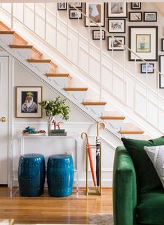 a green couch sitting under a stair case next to a white wall with pictures on it