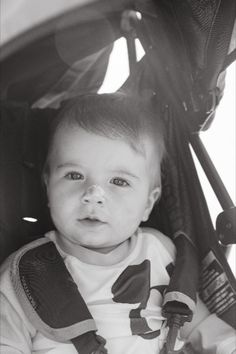 a black and white photo of a baby in a stroller looking at the camera