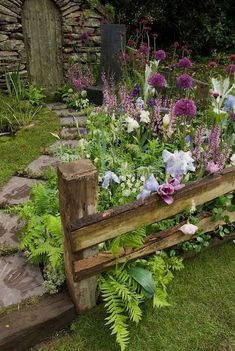 a garden filled with lots of flowers next to a stone wall and wooden bench in the grass