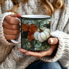 a woman is holding a coffee mug with pumpkins and leaves painted on the inside