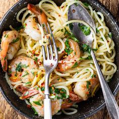 pasta with shrimp and parsley in a black bowl on a wooden table next to silverware