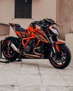 an orange and black motorcycle parked in front of a building