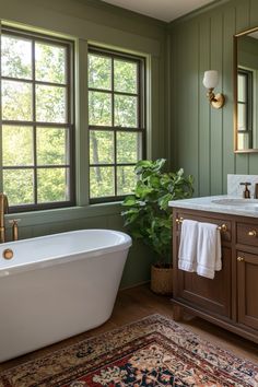 a bath tub sitting next to a window in a bathroom with green walls and wooden floors