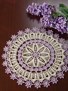 a crocheted doily sits on a table next to purple flowers