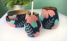 three vases with flowers painted on them sitting on a table next to a potted plant