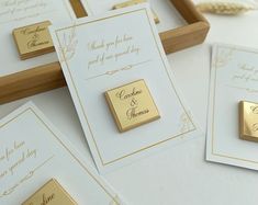 gold and white wedding cards are laying on a table with other items in the background