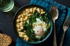 a bowl filled with beans and greens next to bread