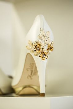 a pair of white high heel shoes with gold flowers on the toes and heels are sitting on a shelf