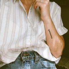 a woman with a small cross tattoo on her left arm, sitting in a chair