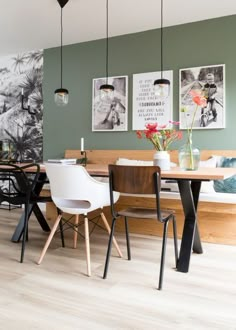 a dining room table with chairs and pictures on the wall above it, along with two vases filled with flowers