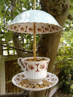 a tea cup and saucer with an umbrella hanging from it's side in front of a tree