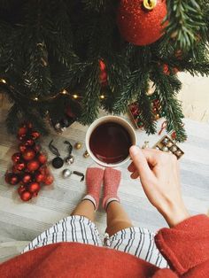 a person sitting in front of a christmas tree holding a cup of coffee