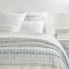 a white bed with blue and green designs on the comforter, pillows and lamps