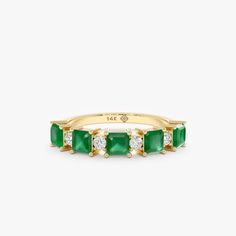 a gold ring with emeralds and diamonds on the sides, set against a white background