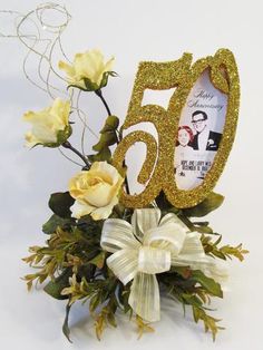 a 50th birthday decoration with flowers and a bow on the top is decorated in gold glitter