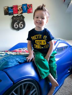 a young boy sitting on top of a blue car bed