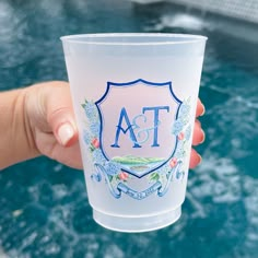 a person holding up a frosted cup with the letters fa on it in front of a swimming pool