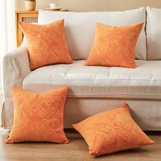 three orange pillows sitting on top of a white couch