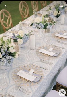 the table is set with blue and white flowers in vases, napkins and place settings