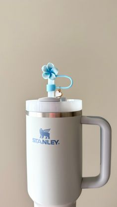 a white coffee cup with a blue flower on the top is shown in front of a beige background