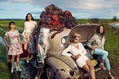 three women are posing in front of an old car with luggage on the hood and back