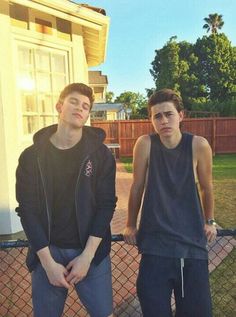 two young men standing next to each other in front of a tennis court and fence