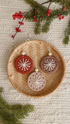 two ceramic ornaments are hanging on a basket with pine branches and red berries in the background