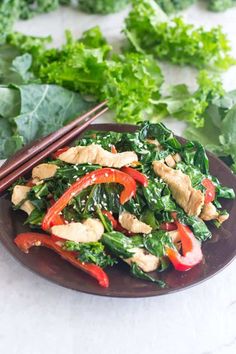 a brown plate topped with chicken and veggies next to chopsticks on a white table