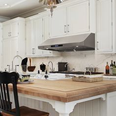 a kitchen with white cabinets and wooden counter tops, an oven hood over the stove