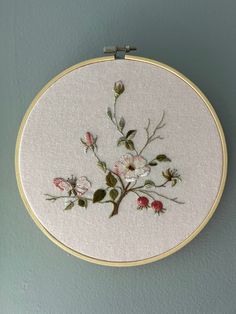 a white embroidery with pink flowers is hanging on the wall next to a gray wall