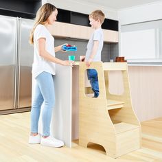 a woman standing next to a child on top of a wooden step stool in a kitchen