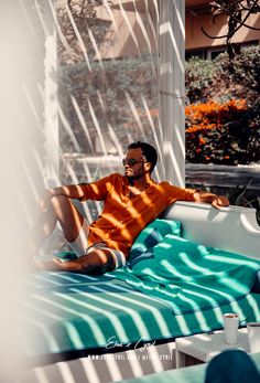 a man sitting on top of a blue and white bed in front of a window