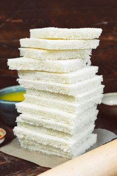 a stack of white cake sitting on top of a wooden table next to a bowl