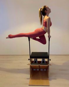 a woman doing an aerial exercise on a stationary machine in front of a white wall