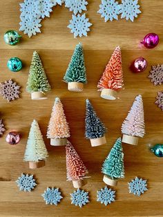 small christmas trees made out of paper on a wooden surface with ornaments in the shape of snowflakes