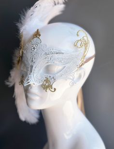 Our women's white laser cut metal masquerade mask, adorned with delicate white feathers and a gold crystal brooch, offers you the opportunity to add a touch of enchanting gold glitter to the mask. Whether you're attending a grand masquerade ball, a themed gala, or simply looking to add a touch of elegance to your attire, this mask ensures you'll be the center of attention. Age Group/Gender - Adult/Women Size/Type - One size fits all adults Mask Color - White Mask Material - Laser cut metal Angel Mask Masquerade Ball, Masquerade Mask With Veil, White Eye Mask Masquerade Mask As Gift, Elegant White Masquerade Mask For Carnival, Elegant White Masquerade Mask For Mardi Gras, White Eye Mask For Masquerade, Elegant White Eye Mask, White Venetian Eye Masquerade Mask, White Venetian Eye Mask For Masquerade