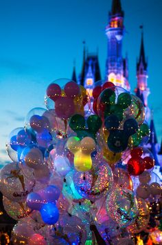 a bunch of balloons that are in front of a castle at night with lights on