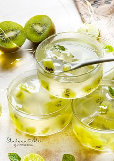 three glasses filled with lemonade and kiwi slices on top of a table next to sliced limes