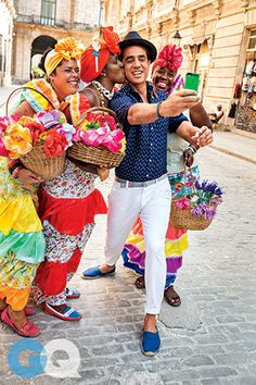 two men taking a selfie with some people dressed in colorful clothing and hats on