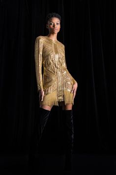 a woman standing in front of a black background wearing a gold dress and thigh high boots