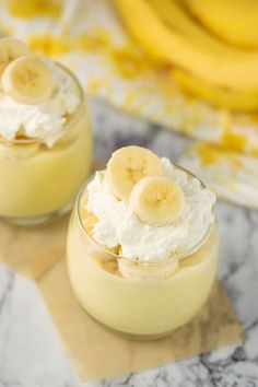 two desserts with banana slices and whipped cream in small glass dishes on a marble surface