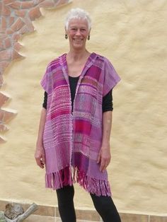 an older woman standing in front of a wall wearing a pink and purple blanket over her shoulders