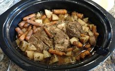 a crock pot filled with meat, potatoes and carrots on top of a table